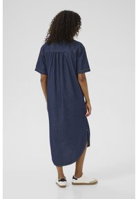 Denim skjortekjole med korte ærmer, en rund kant og sideslids, med en samlet rygdetalje og båret med hvide sneakers.