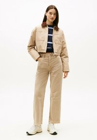 Chaqueta beige recortada con cuello de pana, bolsillos frontales y detalles bordados, combinada con pantalones vaqueros de tiro alto beige y zapatillas blancas.