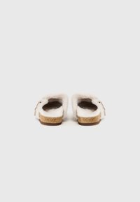 White fluffy slip-on sandals with a cork sole, adjustable strap, and branded detail. Soft texture and open back design for easy wear.