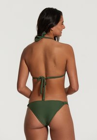Bikini verde con scollo all'americana e design con laccetto sul retro. Presenta un taglio minimalista e una texture liscia, accentuata da dettagli sobri.