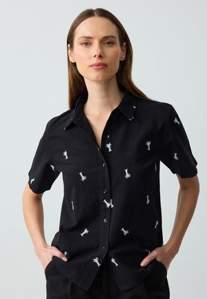 Camicia nera a maniche corte con chiusura a bottoni, caratterizzata da ricami di palme bianche sparsi sul tessuto. Realizzata in materiale leggero.