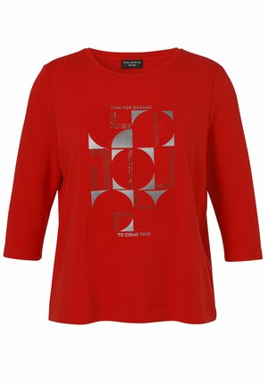 Chemise rouge à manches longues avec un motif géométrique de carrés argentés et rouges et le texte "Il est temps que les rêves deviennent réalité" sur le devant.