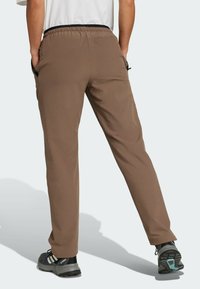 Brązowe spodnie z elastycznym paskiem w talii i bocznymi kieszeniami, charakteryzujące się prostą nogawką i gładką teksturą materiału, w połączeniu z czarnymi butami sportowymi.