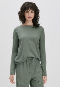 Haut vert à manches longues en tissu doux avec une coupe décontractée, présentant un col large et des coutures d'épaule tombantes.