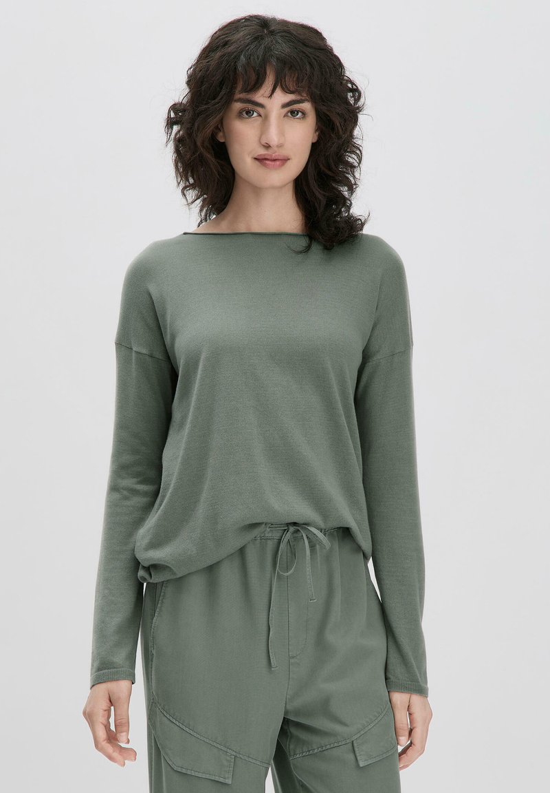 Haut vert à manches longues en tissu doux avec une coupe décontractée, présentant un col large et des coutures d'épaule tombantes.