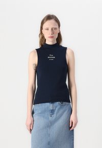 Jūras spēku bez piedurknēm augsts apkakles tops ar baltu "Tommy HILFIGER" logotipu. Gluda auduma, pieguļošs dizains, kombinēts ar gaiši zilu džinsu svārku.