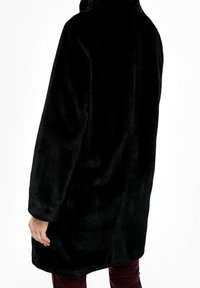 Sort faux fur frakke med høj krave og lange ærmer, der har en blød, fluffy tekstur og en løs pasform. Ingen synlige lukninger.