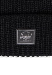 Gorro de lana negro con textura tejida y etiqueta cosida con la marca "Herschel" en blanco sobre un fondo negro.