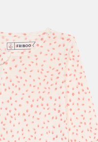 Fehér, hosszú ujjú ing, szétszórt rózsaszín pöttyökkel. Kerek nyakkivágással és méretinformációt tartalmazó címkével látható. Puha pamut anyag.