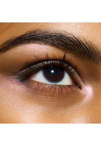 Gros plan sur un œil avec un iris marron foncé, de longs cils et un léger éclat autour de la paupière. La peau a une texture lisse et chaude.