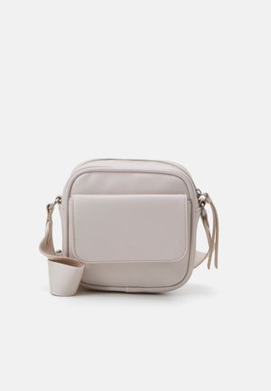 Petit sac bandoulière beige avec poche à rabat sur le devant, fermeture éclair et sangle en tissu ajustable sur fond blanc uni.
