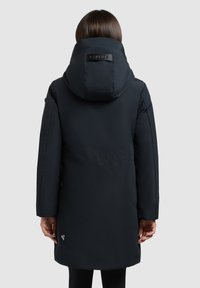 Sort polstret parka med en stor hætte, høj krave og en mærket løkke på bagsiden. Glat tekstur, knælængde og tætsiddende ærmer.