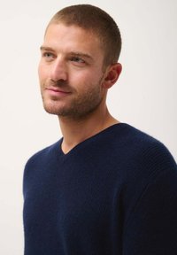 Marineblaues V-Ausschnitt-Pullover aus weichem, strukturiertem Strick. Mittlere Gewicht mit gerippten Akzenten am Ausschnitt und an den Bündchen. Sauberes, minimalistisches Design.