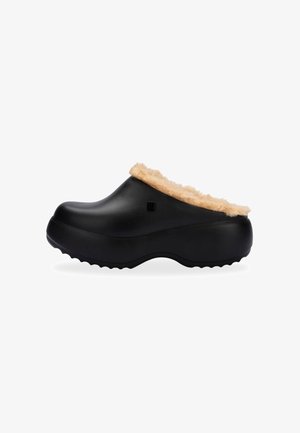 Zueco negro con un suave forro de piel sintética color beige y suela de goma texturizada, que presenta una forma contorneada y un diseño de punta redondeada.