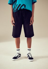 Shorts en jean noir à taille élastique, associés à un t-shirt graphique bleu vif et des baskets noires avec des accents blancs ainsi que des chaussettes rayées.