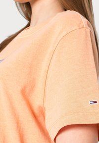 Orange bomull T-shirt med korta ärmar, rundad halsringning och en liten märkeslapp på ärmen. Mjuk textur och avslappnad passform.