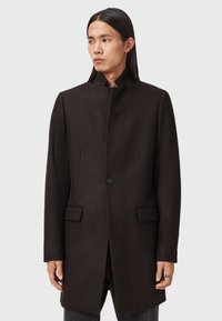 Musta villasekoitteinen takki, jossa on korkea kaulus, yksittäinen nappisulku ja kaksi etutaskua. Sileä pinta ja muotoiltu istuvuus.