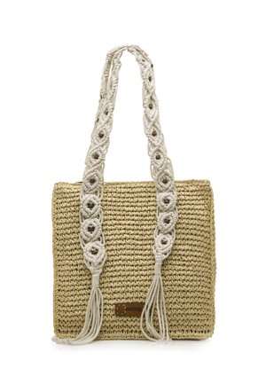 Geflochtene Strohtasche mit cremfarbenen Makramé-Trageriemen, die dekorative Knoten und Quasten aufweist, sowie einem kleinen braunen Logoanhänger auf der Vorderseite.