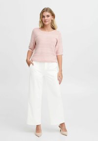 Light pink, textured knit top with three-quarter sleeves and scalloped edges, paired with white wide-leg trousers and nude heels.