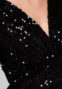 Robe noire à paillettes avec un décolleté en V profond, présentant une surface texturée et réfléchissante créée par de nombreuses petites paillettes rondes.