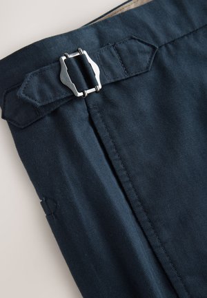 Marineblauer Stoff mit glatter Textur, versehen mit einer silbernen Metall-Schnalle und einem abgesteppten Bund, der das Verschlussdetail hervorhebt.