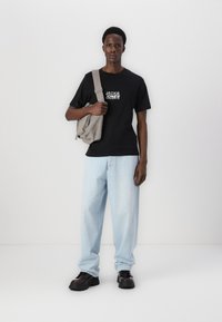 Camiseta negra con "JACK & JONES" impreso en blanco, pantalones vaqueros baggy de color azul claro, y zapatos chunky negros. Bolsa de hombro gris con detalles de cremallera.
