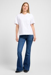 Witte katoenen T-shirt met korte mouwen en een borstzak, gecombineerd met blauwe flared jeans. Eenvoudig ontwerp, casual pasvorm en een gladde textuur.