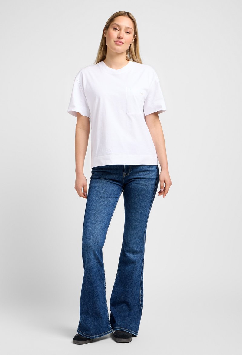 Witte katoenen T-shirt met korte mouwen en een borstzak, gecombineerd met blauwe flared jeans. Eenvoudig ontwerp, casual pasvorm en een gladde textuur.