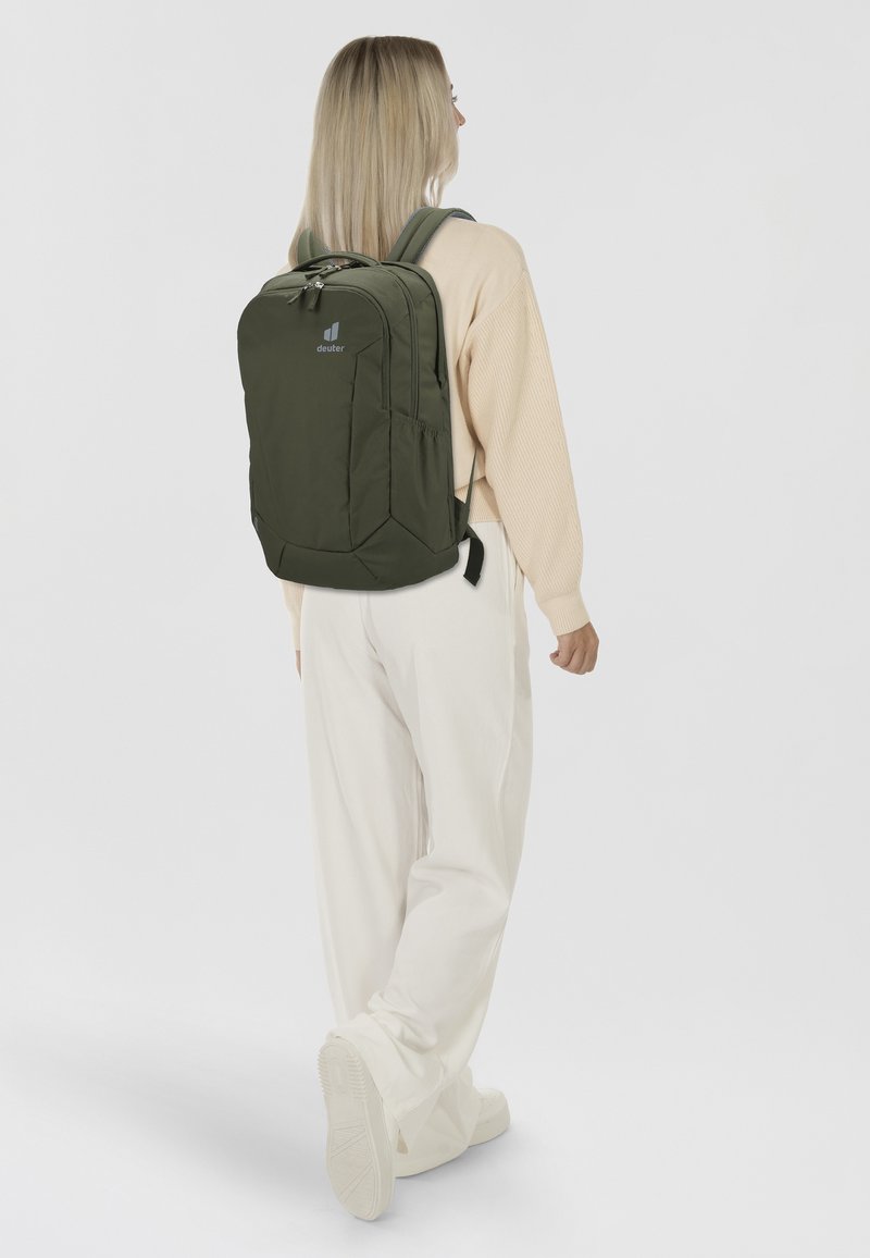Olivgrüner Rucksack mit rechteckiger Form, ausgestattet mit einer vorderen Reißverschlusstasche, verstellbaren gepolsterten Trägern und einem Logo auf der Oberseite.