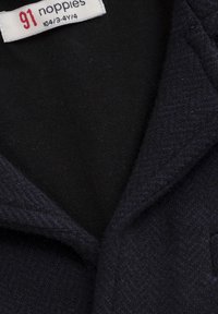 Marineblauw textiel met een visgraatpatroon en een zwarte voering. Het label leest "91 noppies" met zichtbare maatdetails.