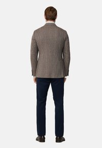 Blazer a scacchi marrone con una vestibilità su misura, spacchetto singolo e rever a punta, abbinato a pantaloni blu navy e scarpe marroni.