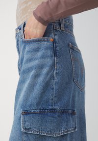 Blue denim cargo pants with multiple pockets, highlighted stitching, and a relaxed fit. Material shows slight wear. Classic design details.