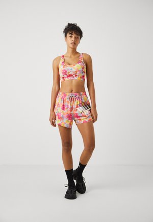Fargerikt sportsett bestående av sportsbh og shortser med blomsterdesign, elastisk midjebånd og logo- detaljer på shortsen. Svarte sko fullfører antrekket.