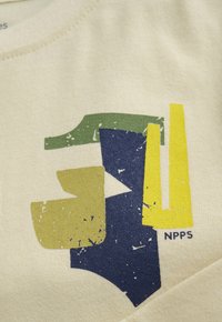 Abstrakte geometrische Formen in Grün, Marineblau, Senfgelb und Gelb auf beigem Stoff mit kleinem "NPPS"-Text in der unteren rechten Ecke.