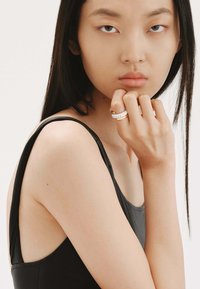 Top negro sin mangas con un brillo sutil. Modelo lleva un anillo dorado y blanco adornado con pequeñas piedras preciosas transparentes en su dedo.