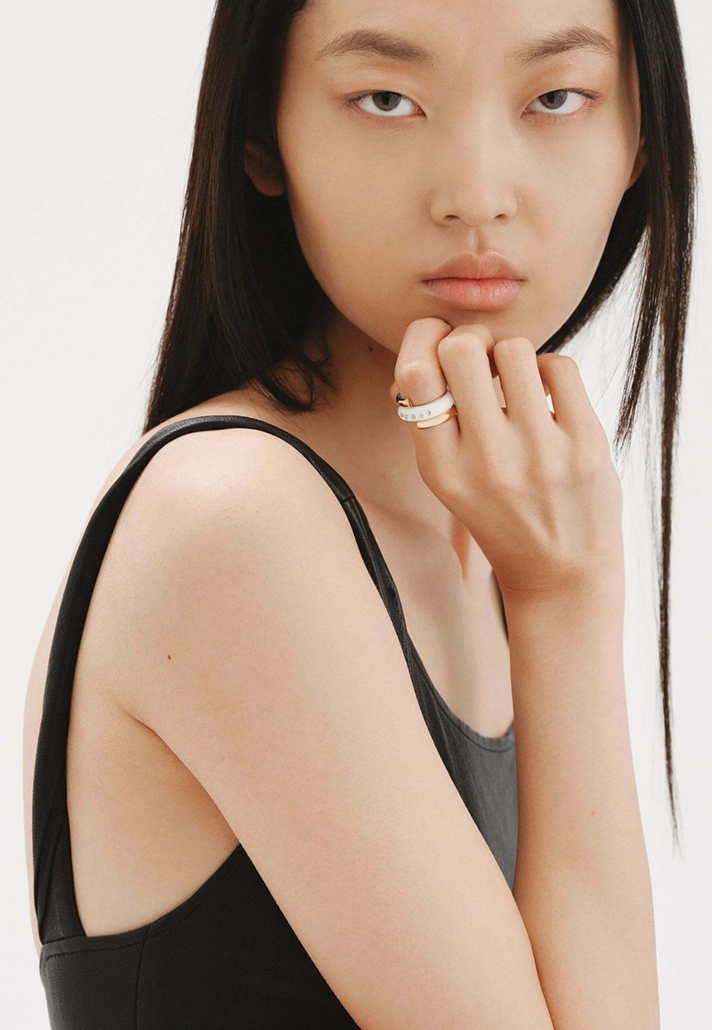 Top negro sin mangas con un brillo sutil. Modelo lleva un anillo dorado y blanco adornado con pequeñas piedras preciosas transparentes en su dedo.