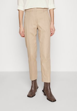 Pantalons beige ajustés en mélange de coton, avec une coupe slim, un devant plat et des passants de ceinture, associés à des bottes chevilles marron foncé.