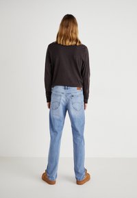 Jeans de mezclilla azul claro con un corte holgado, bolsillos traseros y un parche de cuero marrón. Combinados con una camiseta de manga larga oscura y zapatos marrones.