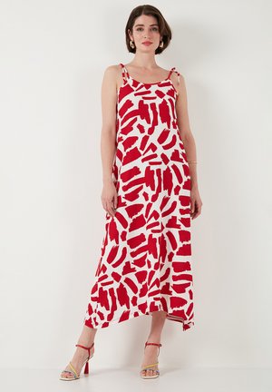 Red and white patterned maxi dress with thin straps, an asymmetric hem, and a flowing design. Paired with multicolored strappy heels.