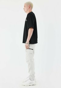 Zwarte katoenen t-shirt met korte mouwen, gecombineerd met lichtgrijze cargobroek met ritszakken, en witte sportschoenen.