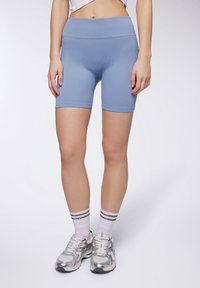 Shorts da bici a costine azzurro chiaro con vita alta, caratterizzati da una texture liscia e un design aderente, abbinati a scarpe sportive argentate e calzini a righe.