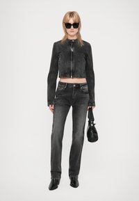 Jaqueta de denim preta cropped com fecho frontal e detalhes de costura, combinada com jeans pretos de corte direito. Os acessórios incluem óculos de sol pretos e uma mala.