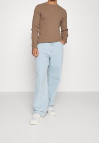 Brun ribbade tröja, ljusblå vida jeans och vita sneakers. Synliga fickor och rena sömmar på byxorna. Neutral färgpalett.