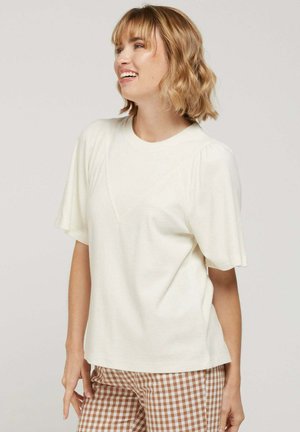 Top crème à manches courtes en tissu doux avec un col rond et de subtils détails froncés sur les manches, associé à un pantalon à carreaux marron.