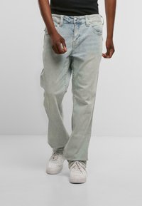 Heledad sinised denim teksad, vabalt istuvad, koos nööbiga sulgemise, viie tasku ja kergelt pleekinud välimusega, kantud koos valgete tennisereitega.
