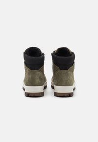 Stivaletti alla caviglia in suede verde con colletto lavorato a maglia nera, suola bianca e suola in gomma marrone con trazione. Presentano cuciture minime e accenti di logo.