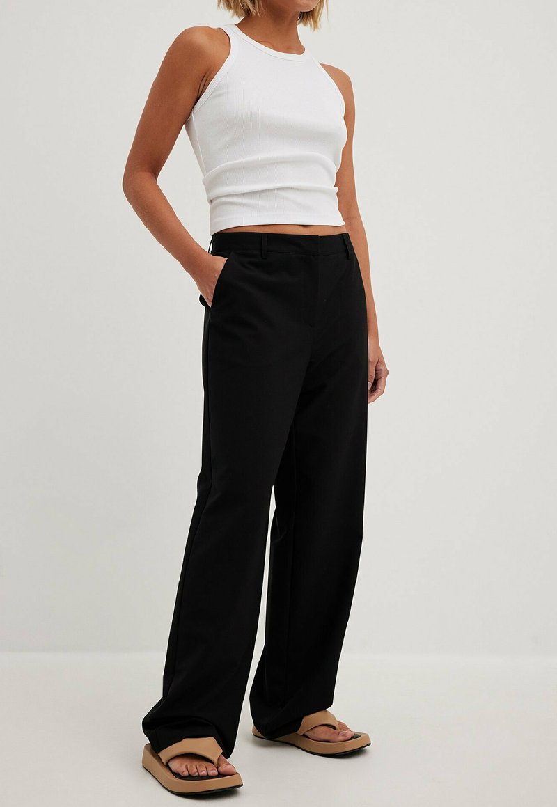 Pantalons larges noirs avec une texture lisse, dotés de poches latérales et d'une taille ajustée, associés à un débardeur en coton blanc à côtes.