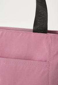 Rosa stoff tote bag med matt finish, med svarte vevde håndtak og en fronlomme med sømte kanter. Enkelt, funksjonelt design.