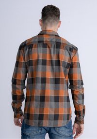 Męska koszula flanelowa w pomarańczowo-szaro-czarną kratę, z mankietami na guziki i zakrzywionym dołem, wykonana z miękkiego, teksturowanego materiału.