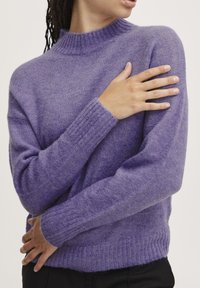 Lilla strikket sweater med høj hals og ribbede manchetter. Blød tekstur, afslappet pasform og minimale designdetaljer.